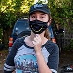 Paola Beck Gisler stands wearing a black mask with a yellow smile.